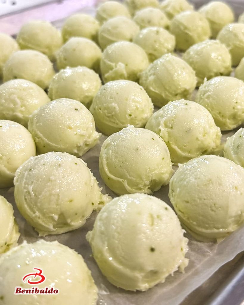 Rows of pale green pistachio ice cream scoops on a parchment-lined tray, speckled with tiny green bits.