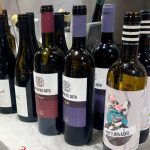 Row of wine bottles on a marble counter in a store, with purple and burgundy foil capsules.