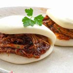 Steamed bao buns with glossy braised meat filling and a sprig of parsley on top.