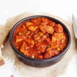 Hearty tomato-based stew with chunky meat and vegetables in a dark bowl on a rustic burlap background, Benibaldo logo visible.